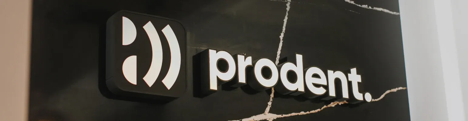Przestrzenne białe logo prodent. na ścianie z czarnego marmuru z jasnymi żyłkami.